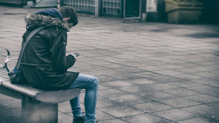 Ragazzo consulta smartphone seduto su una panchina