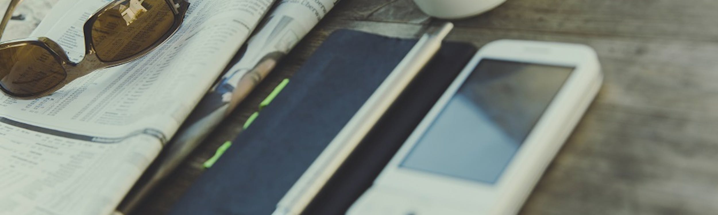 Smartphone e quotidiano su tavolo con caffé